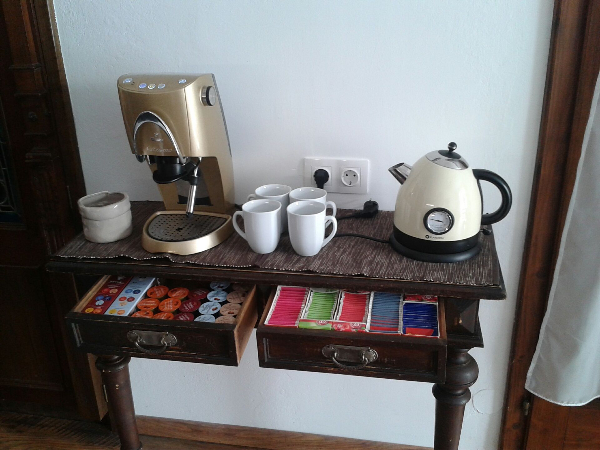 Kaffeemaschine und Wasserkocher auf einem Tisch mit Tassen und Teebeuteln.