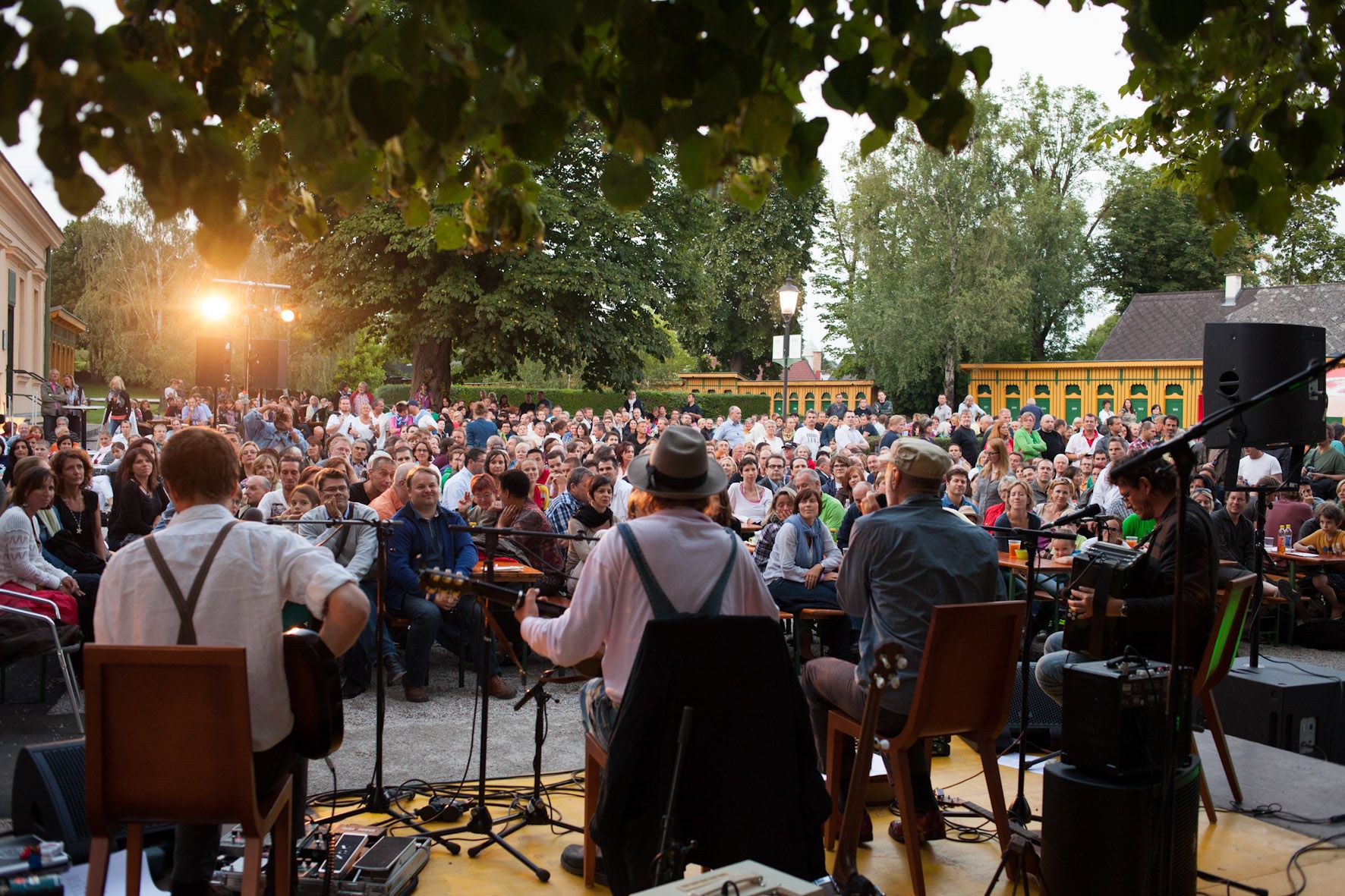 Open-Air-Konzert mit Musikern auf einer Bühne und einem großen Publikum im Freien.