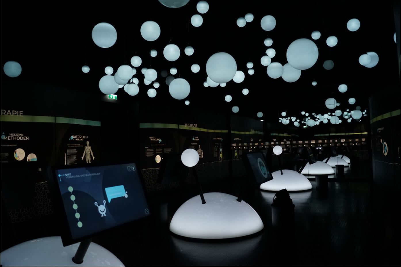 Dunkler Ausstellungsraum mit leuchtenden Kugeln und interaktiven Bildschirmen.
