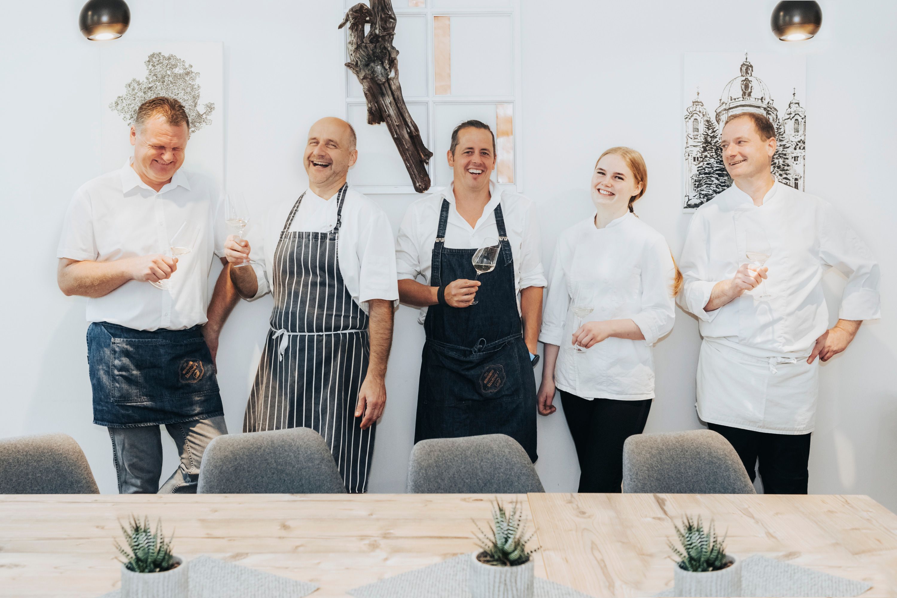 Fünf Personen in Kochkleidung lachen und halten Weingläser in der Hand.