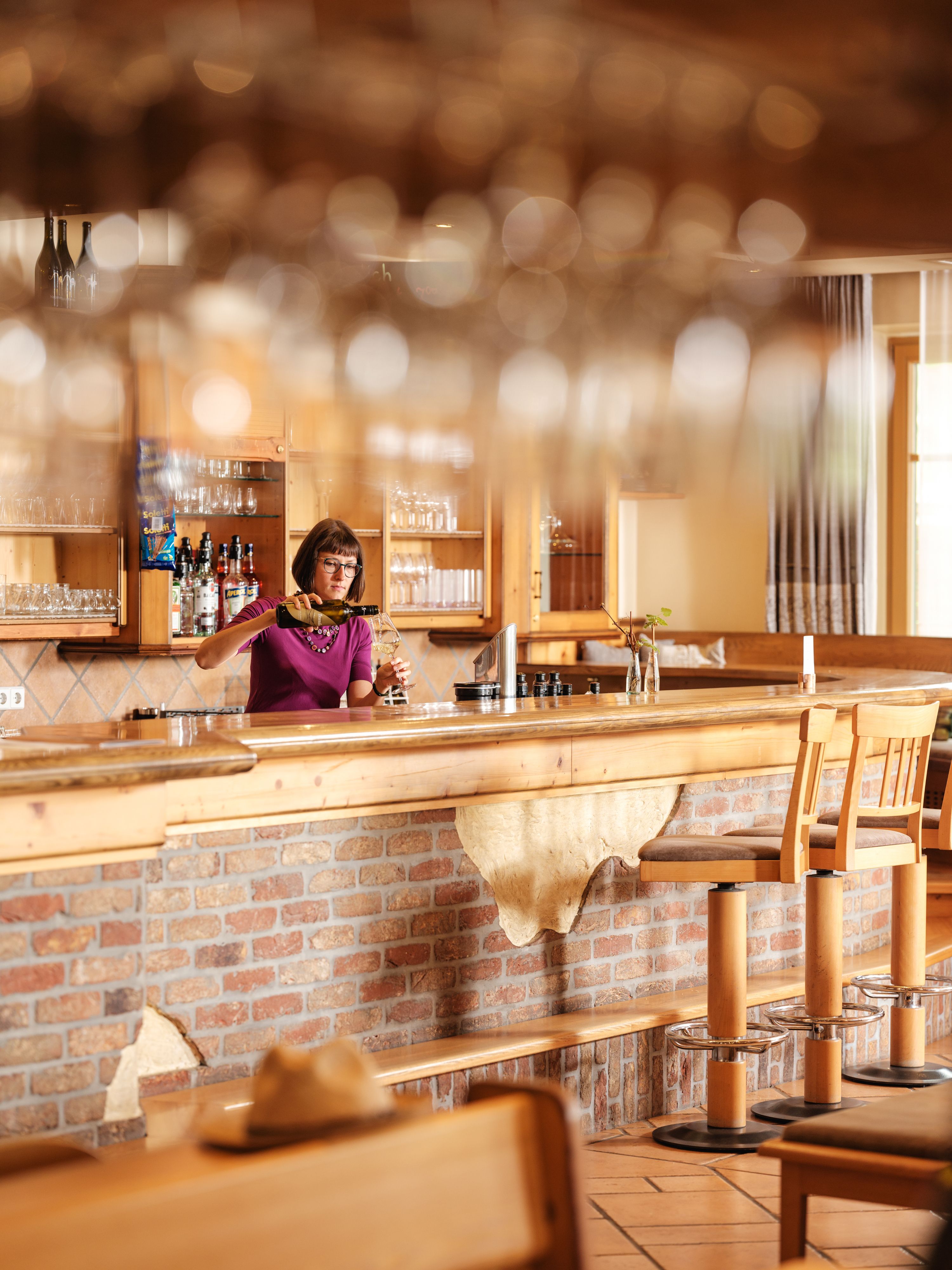 Eine Frau steht hinter einer Bar in einem rustikalen Restaurant und schenkt Wein ein.