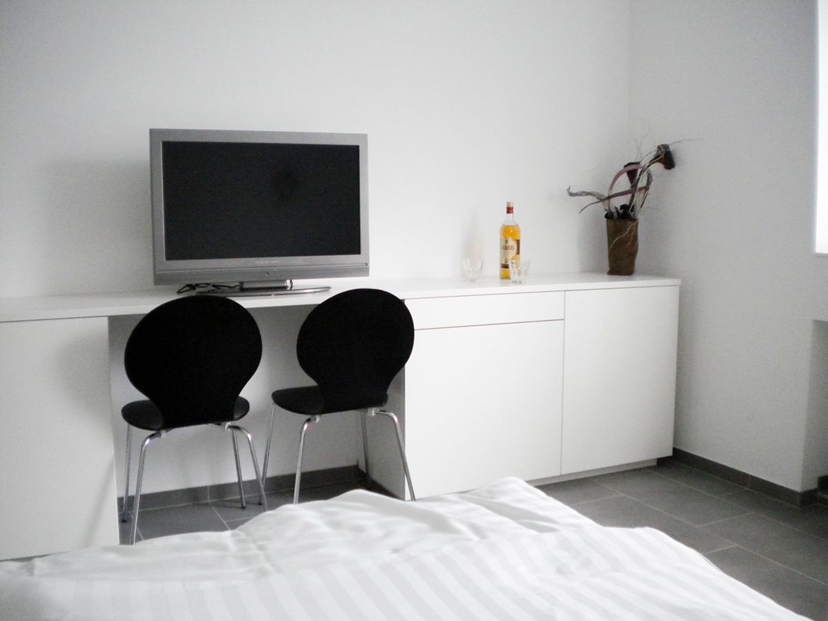 Modernes Zimmer mit Fernseher, zwei schwarzen Stühlen und weißem Schrank.