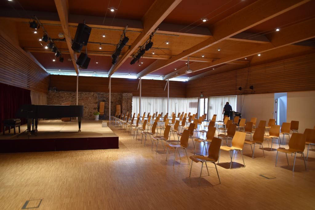 Ein leerer Veranstaltungssaal mit Stühlen und einem Flügel auf der Bühne.