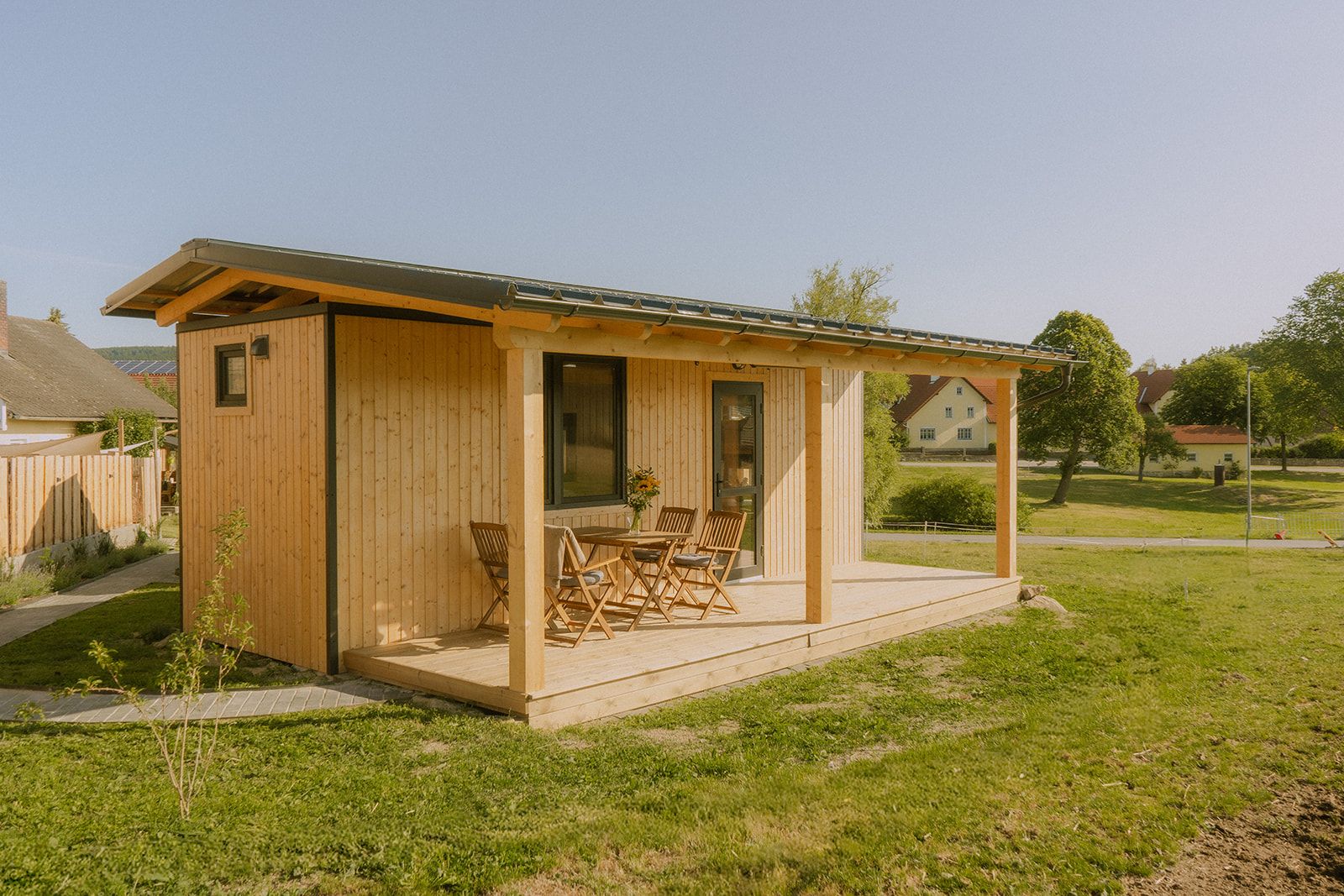 Ein kleines Holzhaus mit Veranda und Gartenmöbeln in einer ländlichen Umgebung.