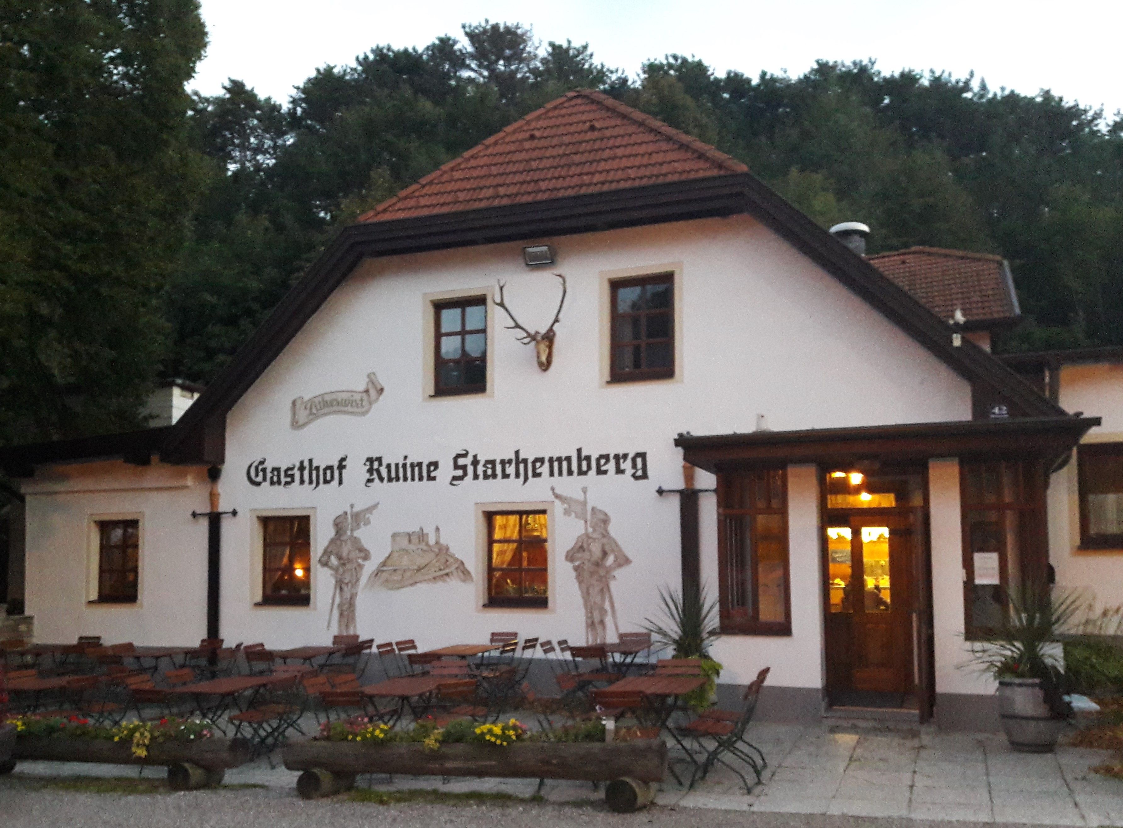 Ein traditionelles Gasthaus mit Außenbereich und Wandmalereien, umgeben von Bäumen.