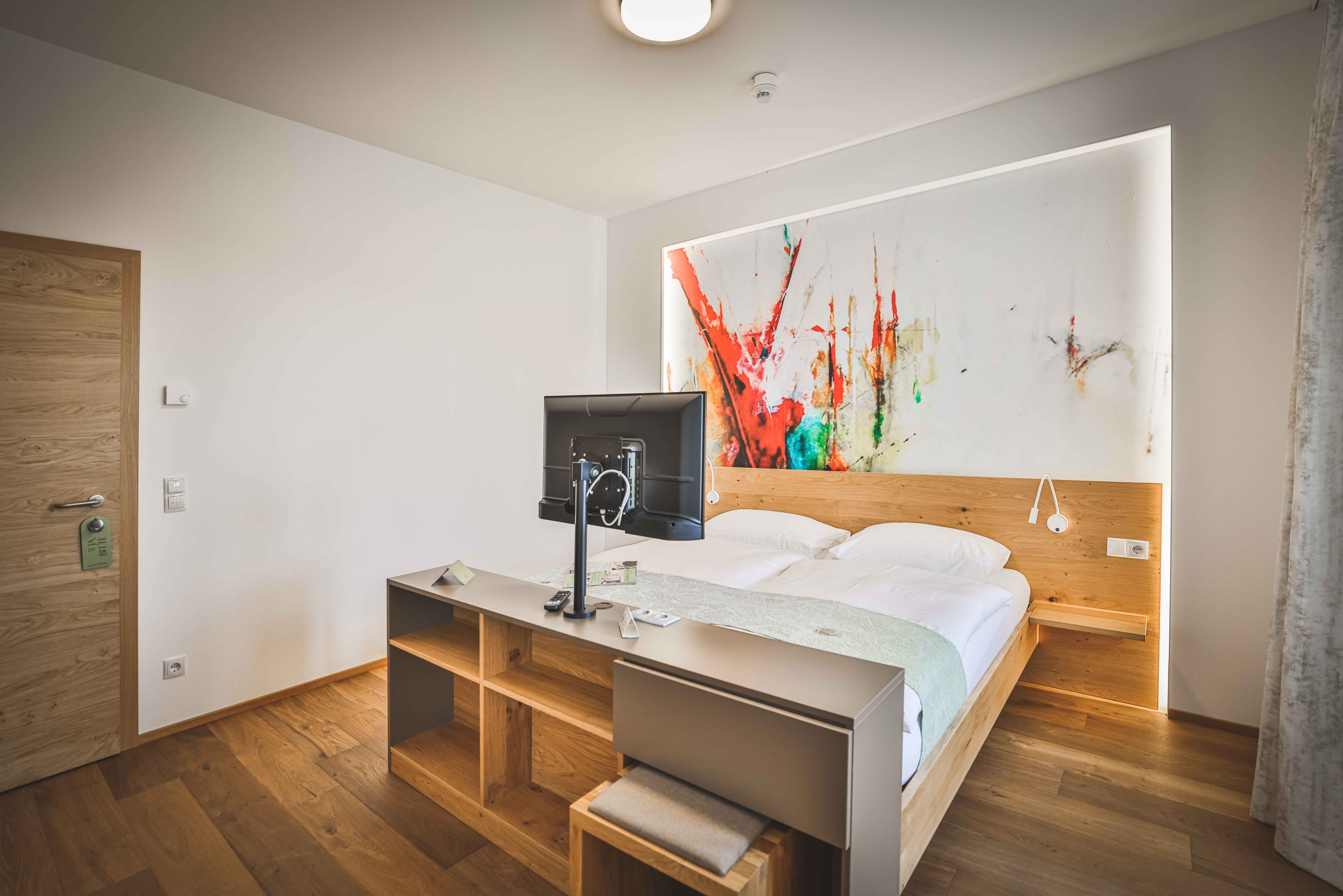 Modernes Hotelzimmer mit Doppelbett, abstraktem Kunstwerk an der Wand und Fernseher auf einem Tisch.