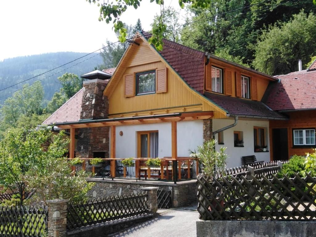 Ein traditionelles Ferienhaus mit Holzveranda und Schindeldach, umgeben von Bäumen und Bergen.