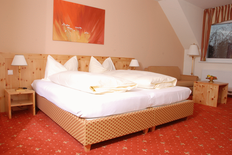 Gemütliches Hotelzimmer mit Doppelbett, Holzmöbeln und rotem Teppich.