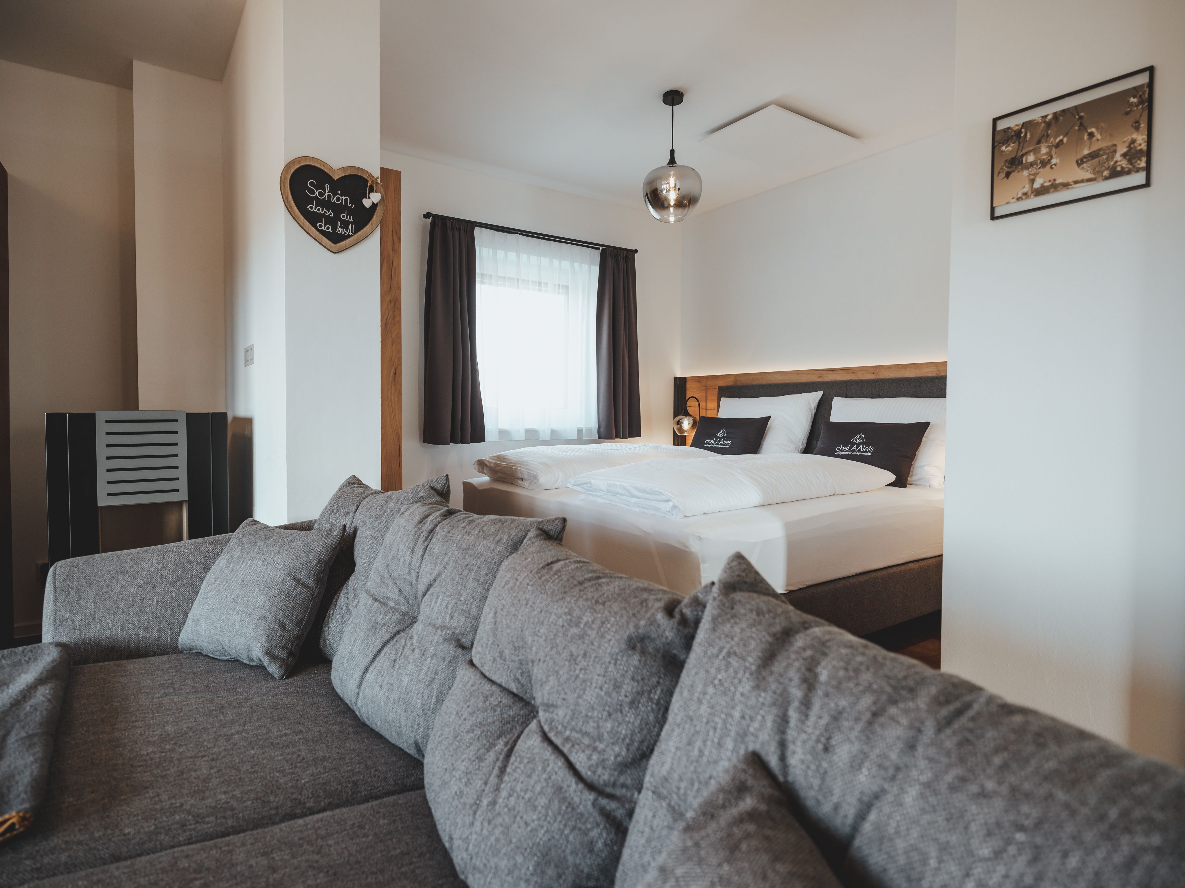 Modern eingerichtetes Schlafzimmer mit grauem Sofa und Doppelbett.