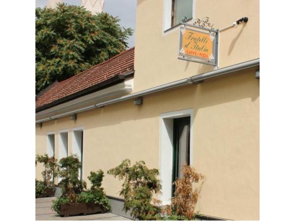 Außenansicht eines gelben Gebäudes mit einem Schild "Fratelli d'Italia Caffè-Pizza" und Pflanzen vor der Fassade.