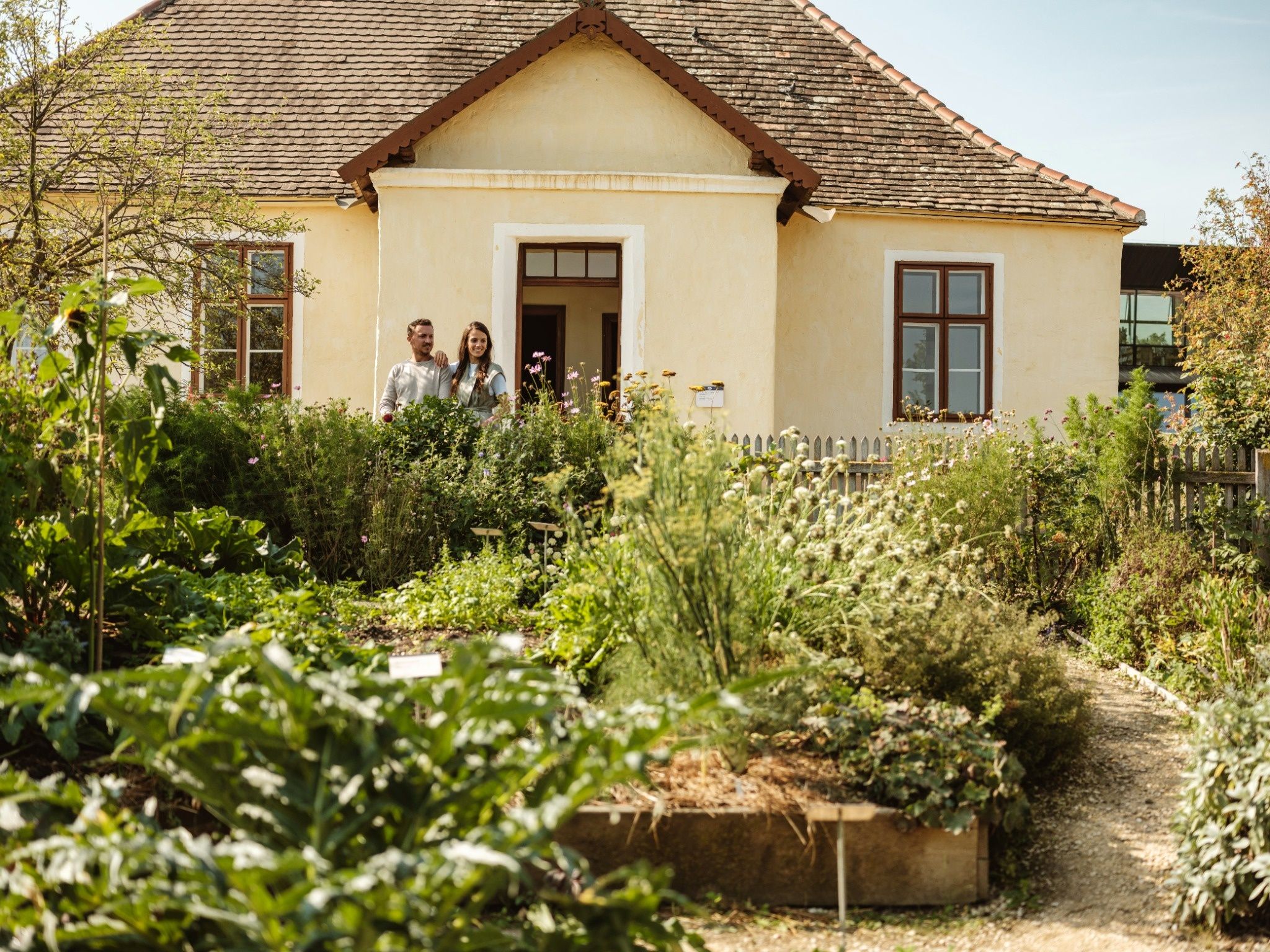 Paar steht vor einem historischen Haus im Weinviertler Museumsdorf Niedersulz, umgeben von einem blühenden Garten.