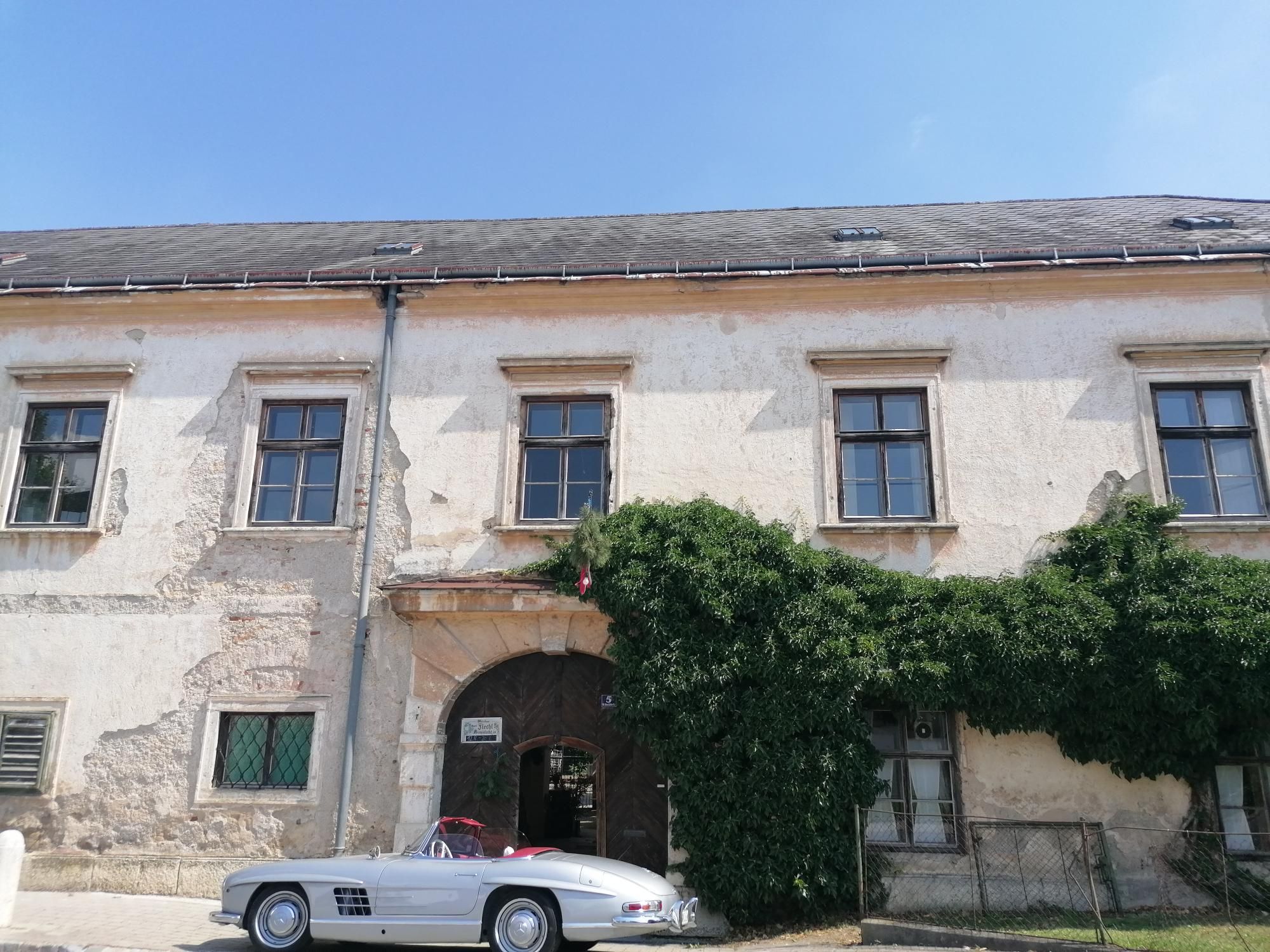 Altes Gebäude mit Efeu bewachsen und einem klassischen weißen Auto davor.