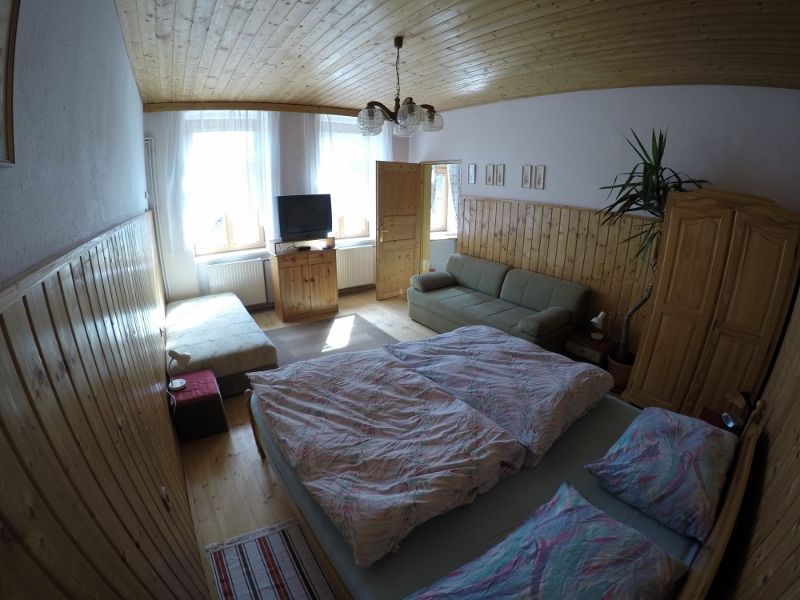 Gemütliches Schlafzimmer mit Doppelbett, Sofa, TV und Holzmöbeln in einer Ferienwohnung.