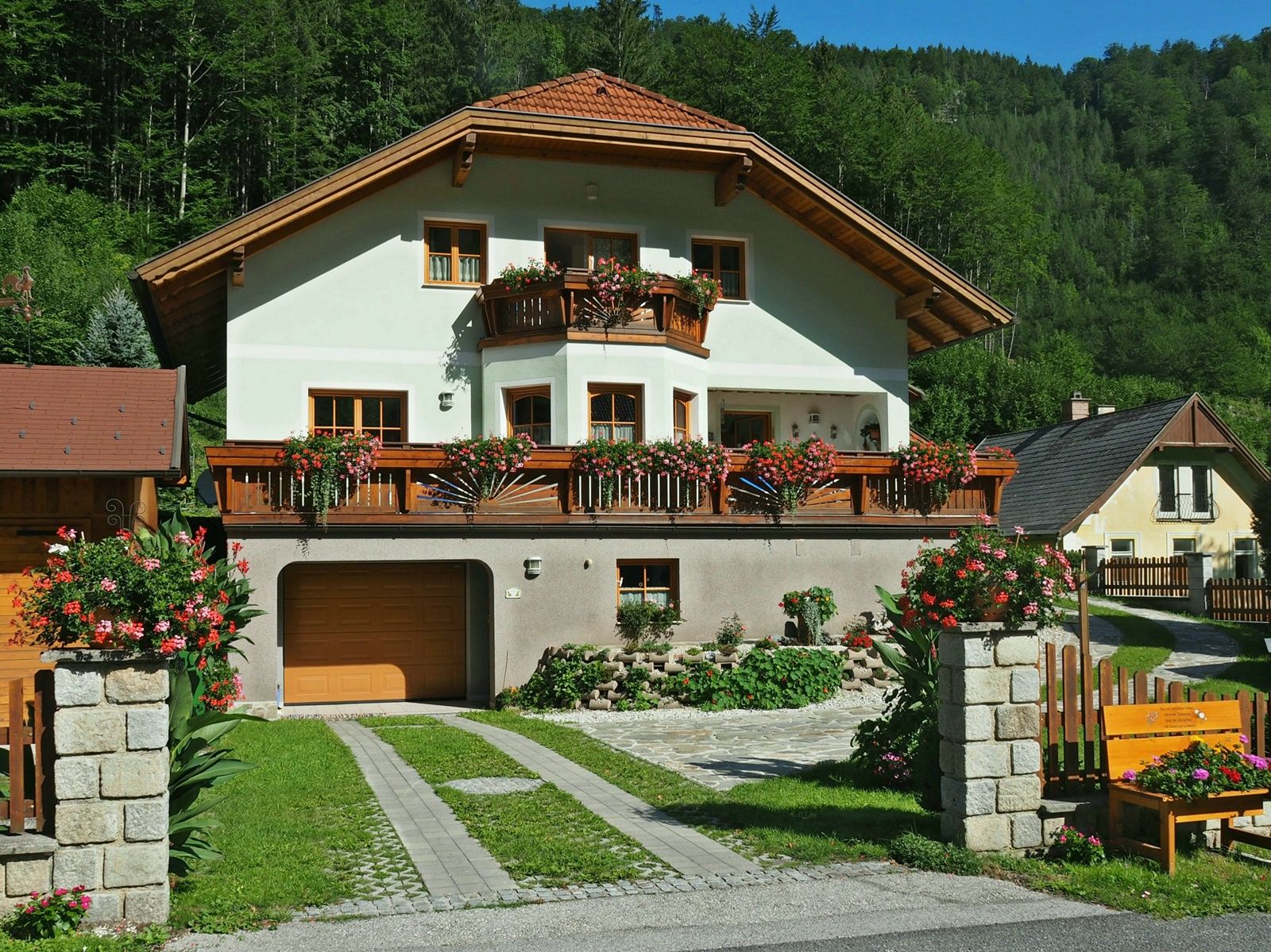 Ein zweistöckiges Haus mit Holzbalkonen und Blumen, umgeben von grüner Landschaft.