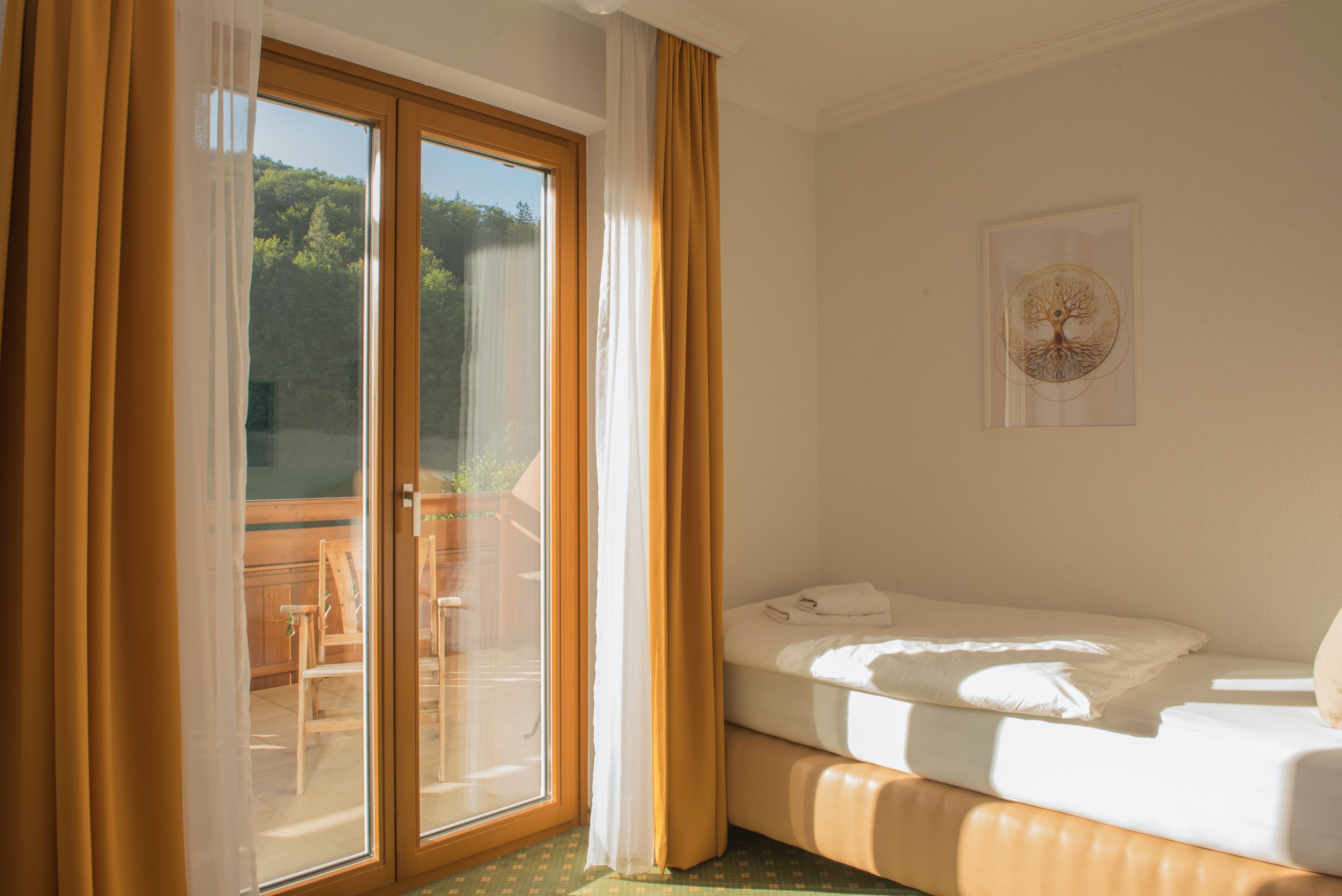 Einzelzimmer mit Balkon, Bett, gelbe Vorhänge, Holzbalkon, sonnig.