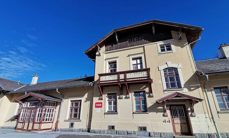 Historisches Bahnhofsgebäude mit gelber Fassade und rotem Holzdekor unter blauem Himmel.