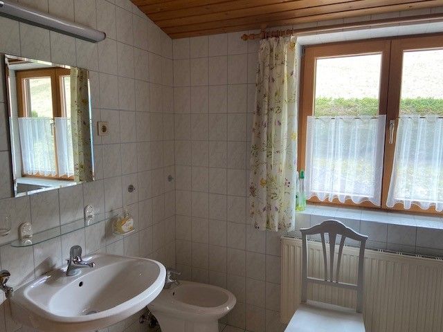 Ein Badezimmer mit Waschbecken, Bidet, Spiegel und Fenster mit Vorhängen.