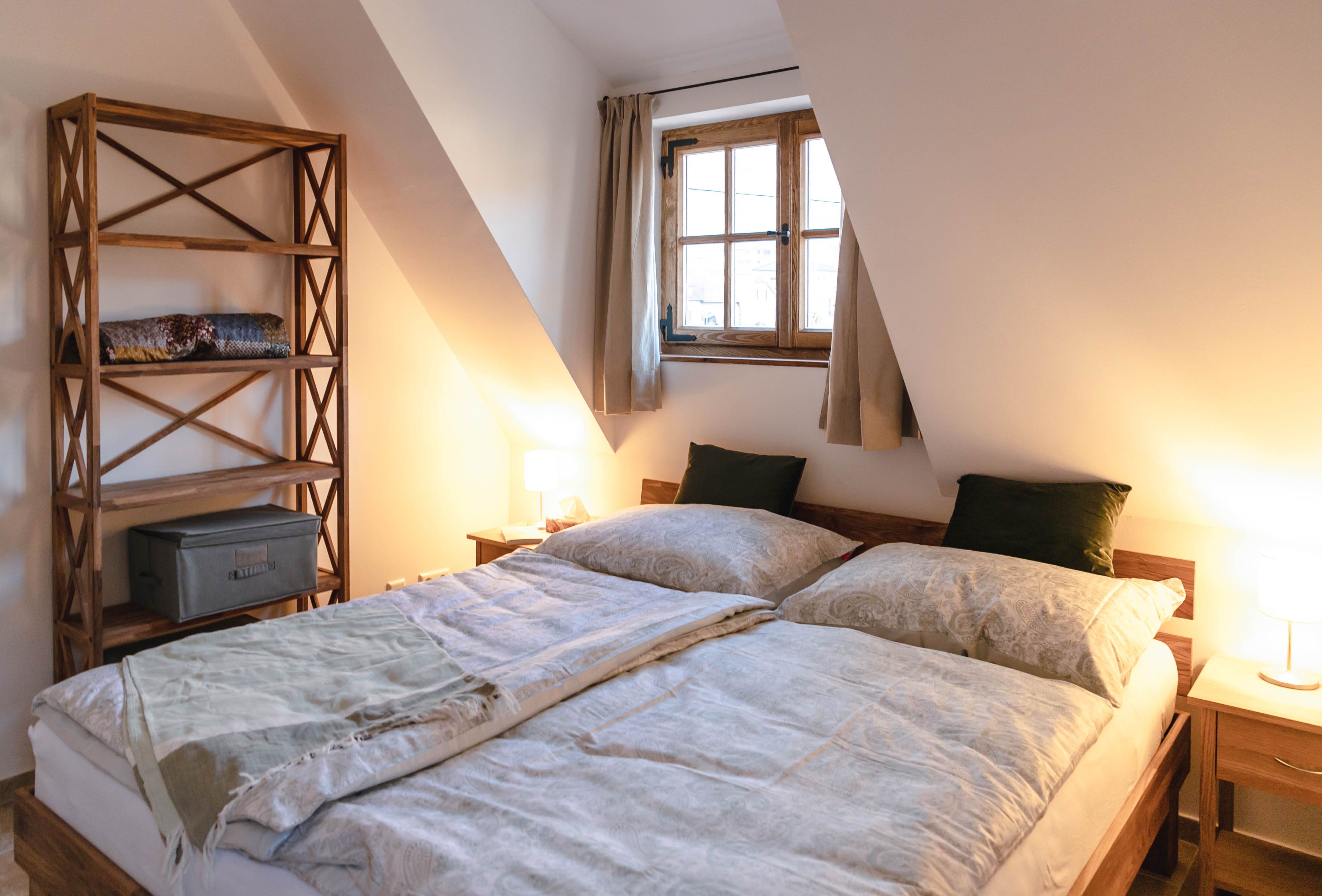 Gemütliches Schlafzimmer mit Doppelbett, Holzbücherregal und Fenster mit Vorhängen.