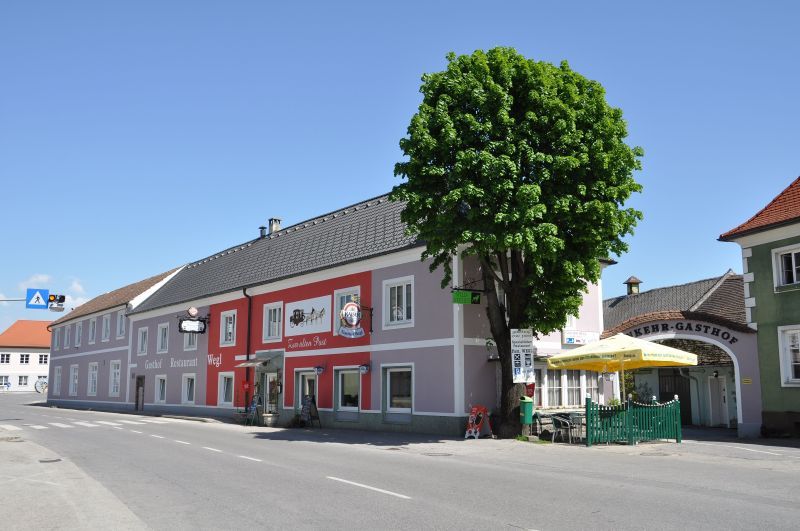 Gasthof Wegl an einer Straße mit Baum und Sonnenschirmen.