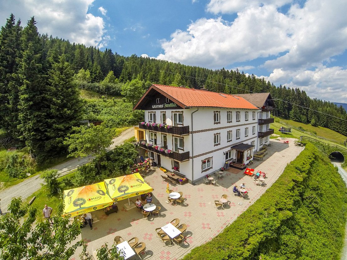 Alpengasthof mit Terrasse und Sonnenschirmen in bergiger Landschaft.