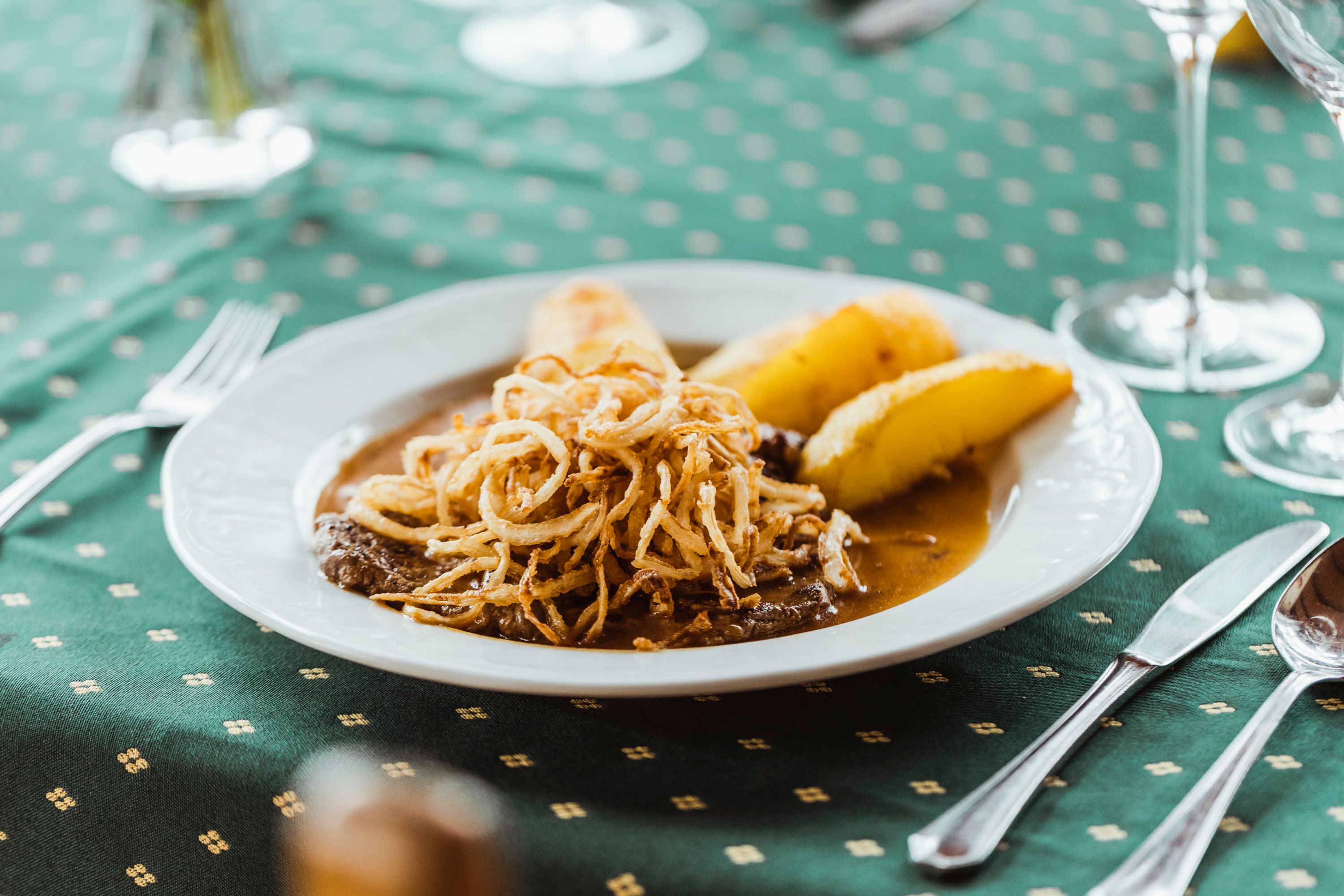 Ein Teller mit Zwiebelrostbraten und Braterdäpfeln auf einem grünen Tisch.
