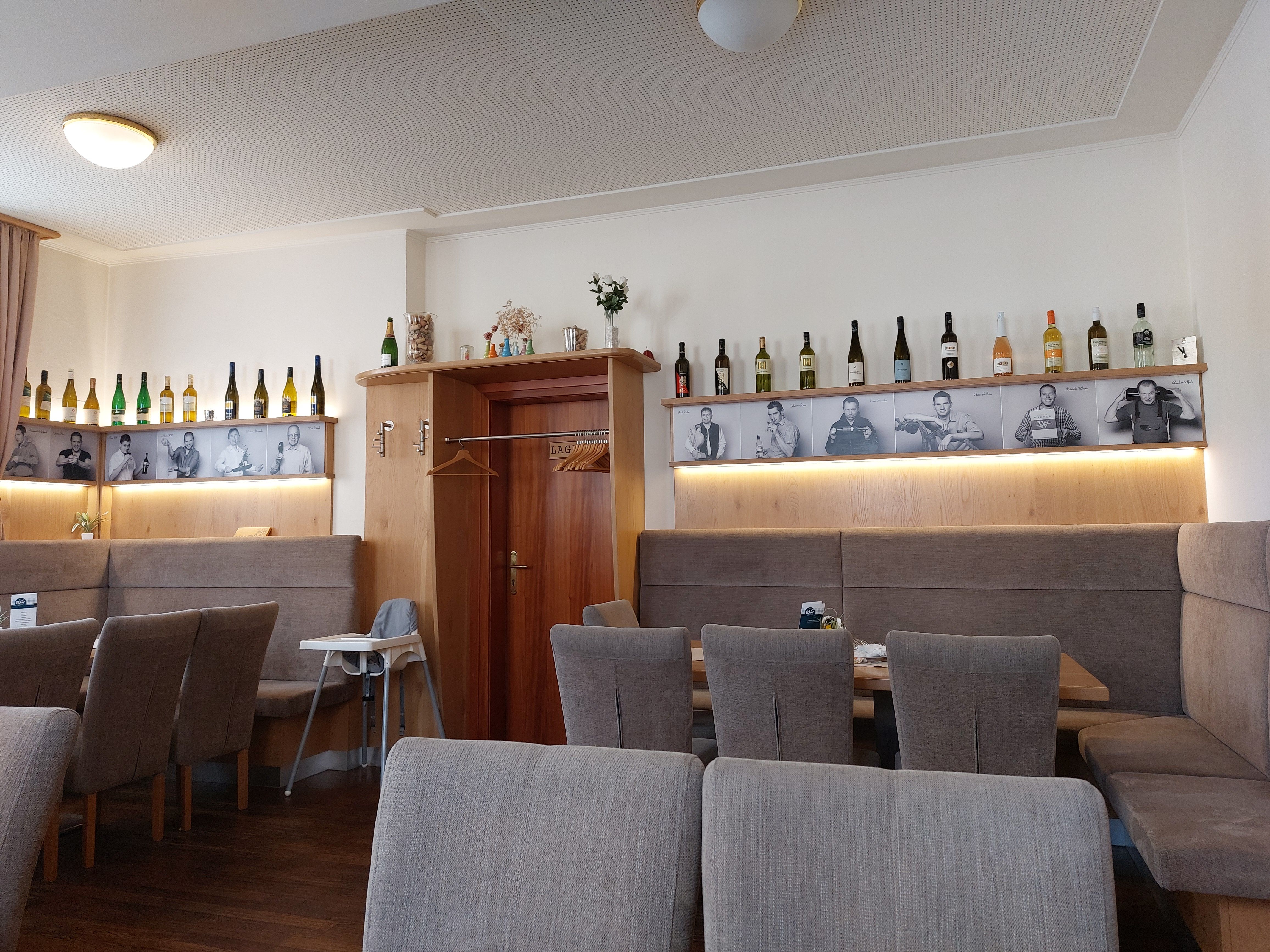 Innenansicht eines Restaurants mit Weinflaschen und Schwarz-Weiß-Fotos an der Wand.