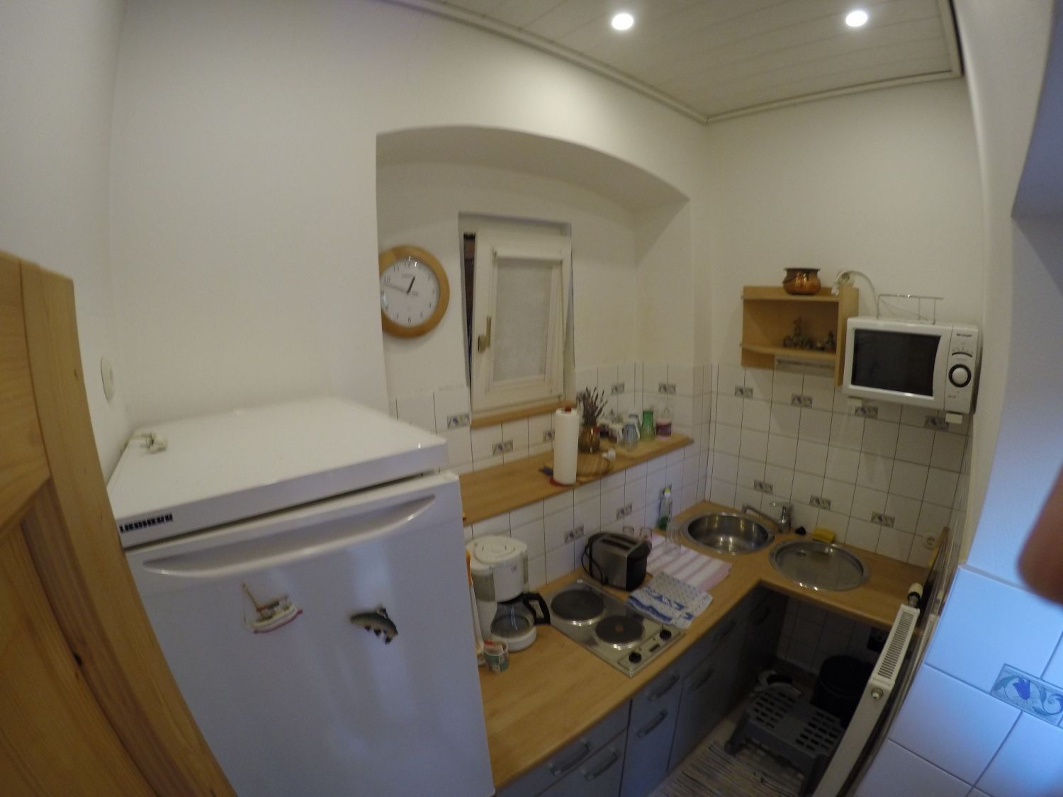 Kleine Küche mit Kühlschrank, Mikrowelle, Herd und Spüle.