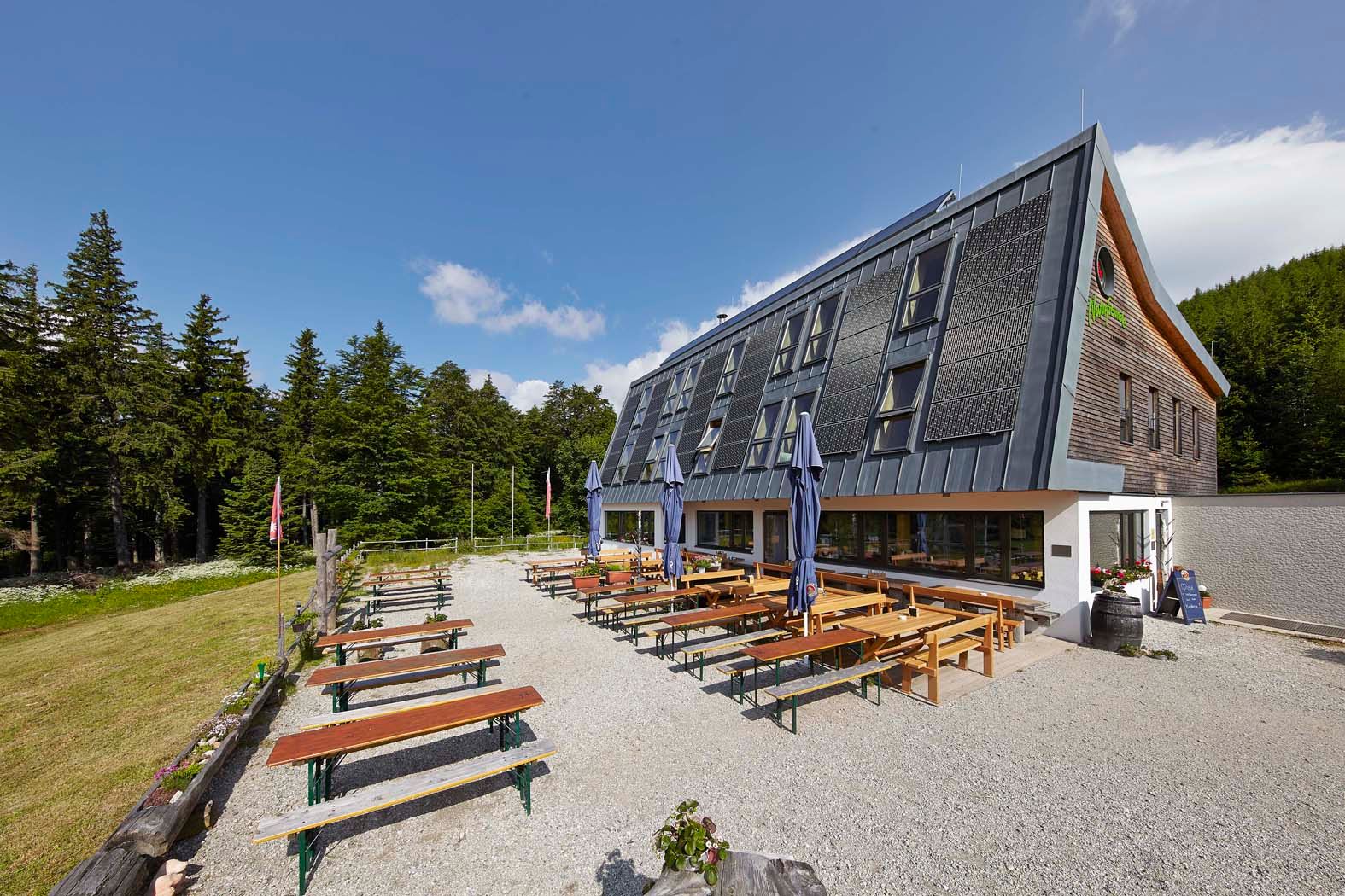 Ein modernes Gebäude mit Solarpanelen und Biergarten im Freien, umgeben von Wald.