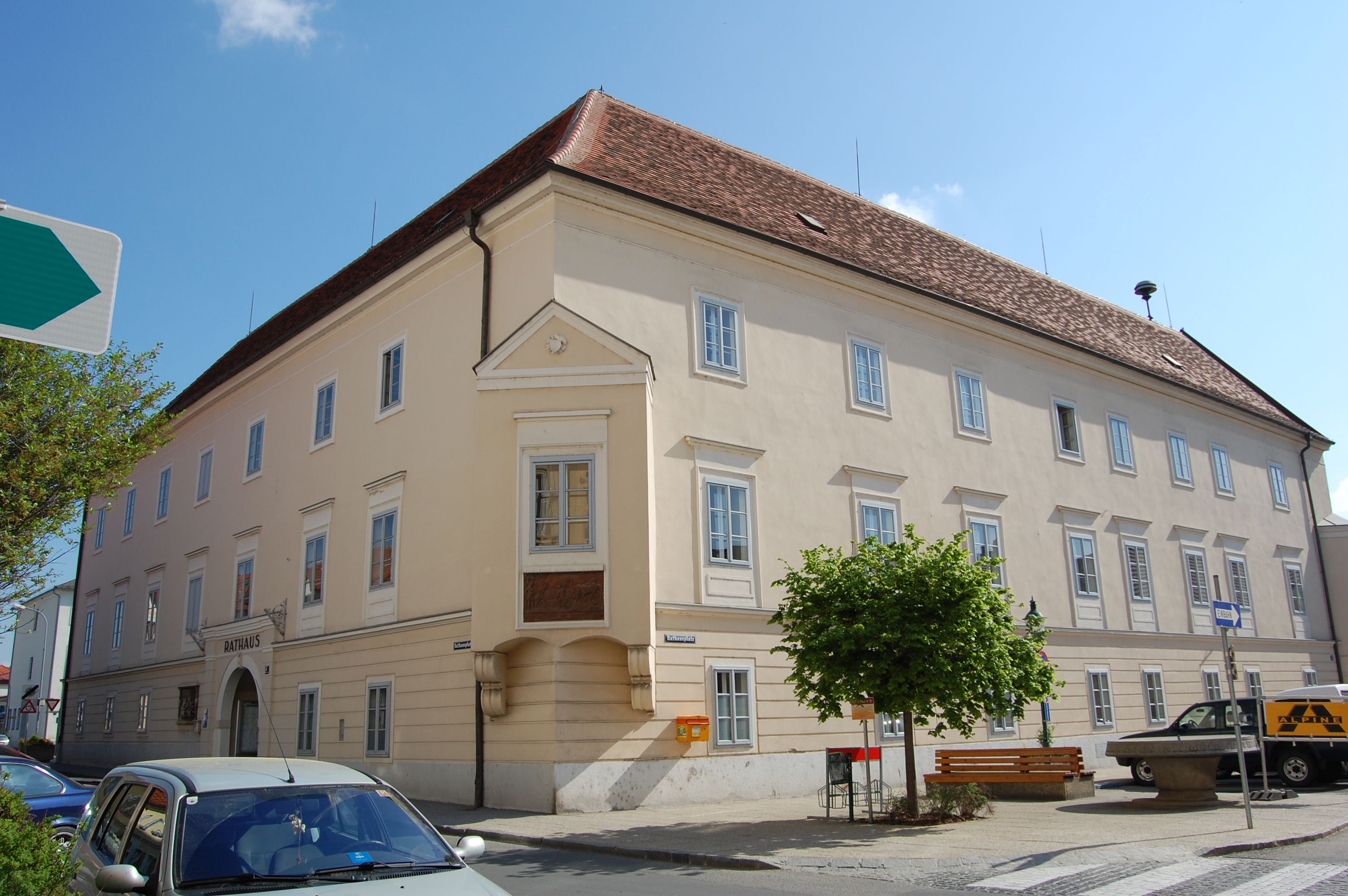 Ein großes, helles Gebäude mit roten Dachziegeln und vielen Fenstern, beschriftet mit 'Rathaus'.