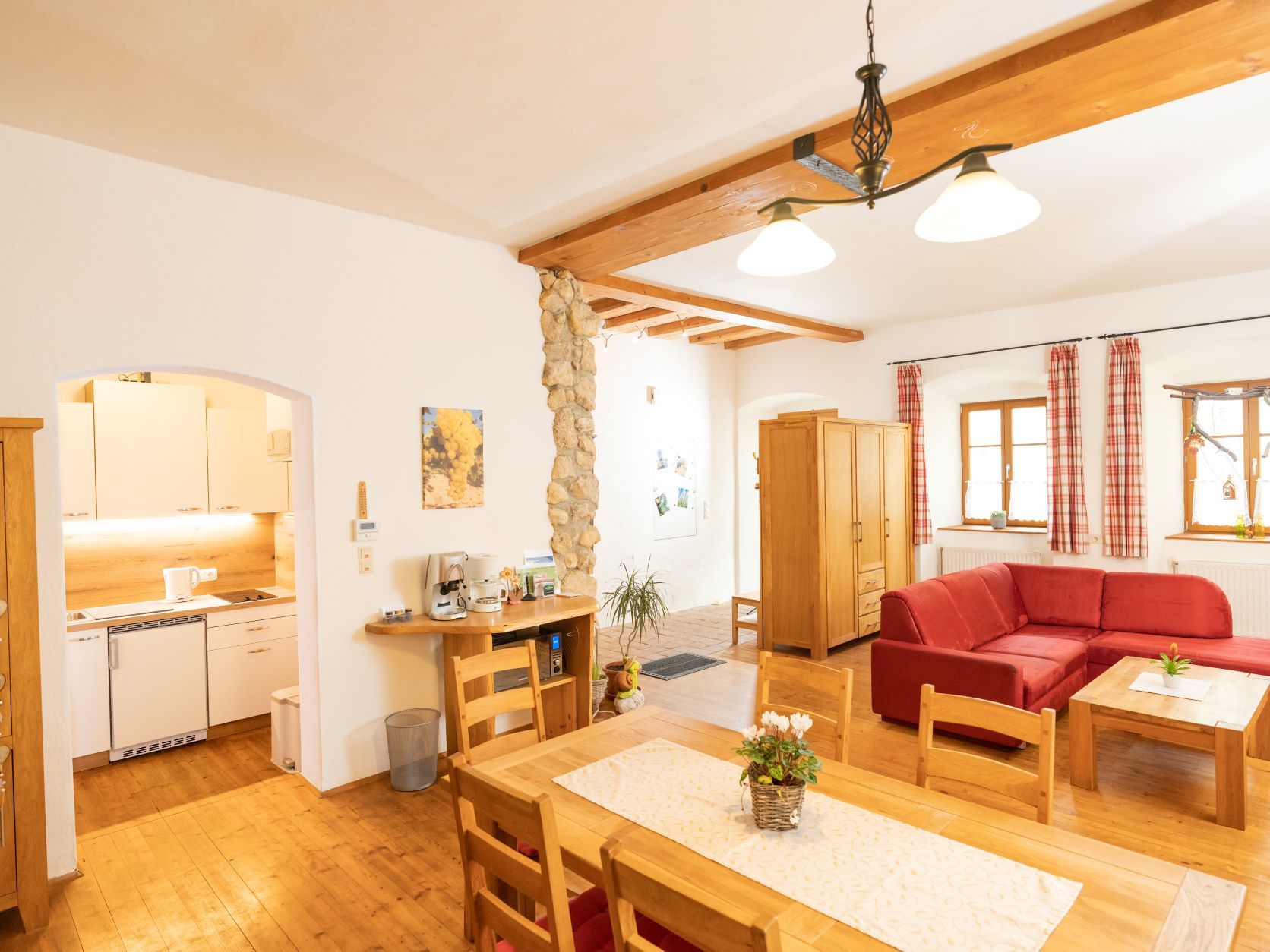 Gemütliches Wohnzimmer mit Holzmöbeln, rotem Sofa und offener Küche.