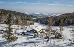 Skigebiet mit Sessellift und Skifahrern, umgeben von schneebedeckten Bäumen und Hügeln.