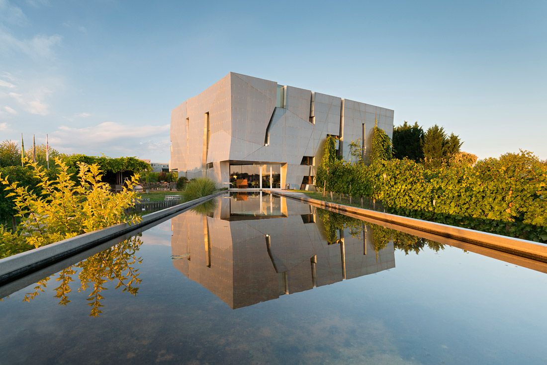 Modernes Gebäude der Loisium WeinWelt mit reflektierendem Wasserbecken im Vordergrund.