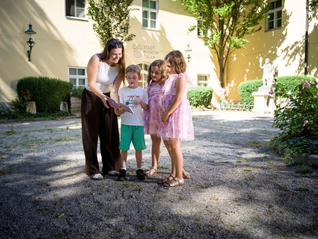 Eine Frau und drei Kinder stehen vor dem Stadtmuseum Tulln und lesen im Folder