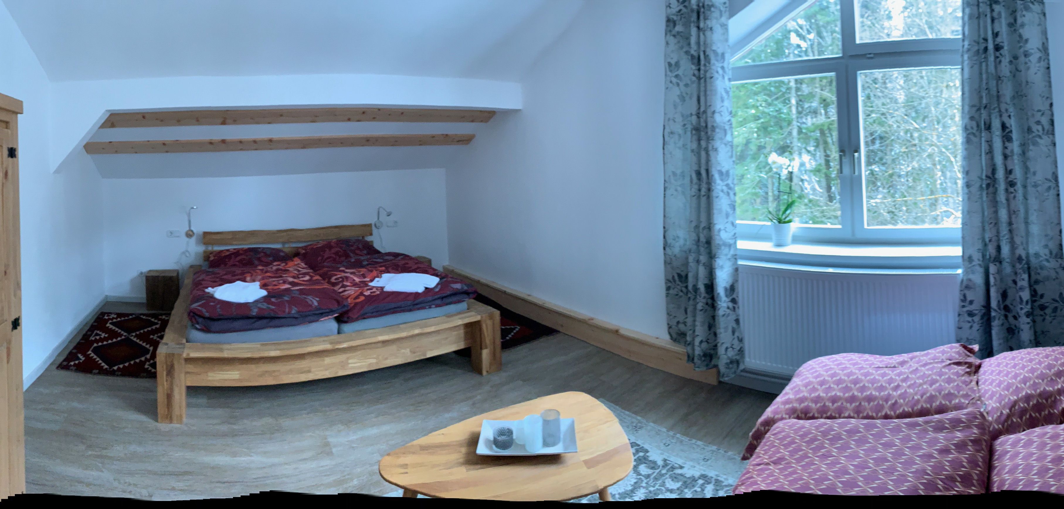Gemütliches Schlafzimmer mit Holzbett, Sofa und großem Fenster mit Vorhängen.