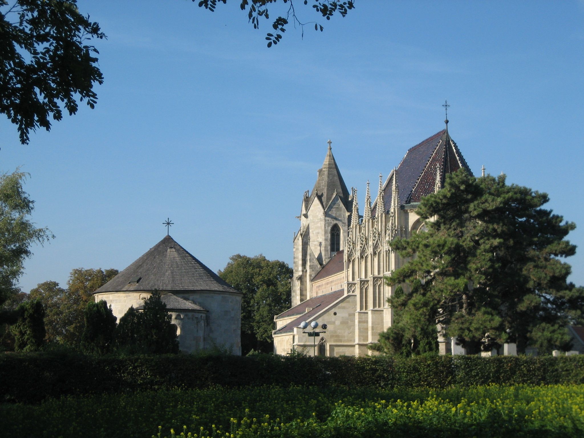 Marienkirche in Bad Deutsch-Altenburg mit blauem Himmel und Bäumen im Vordergrund.