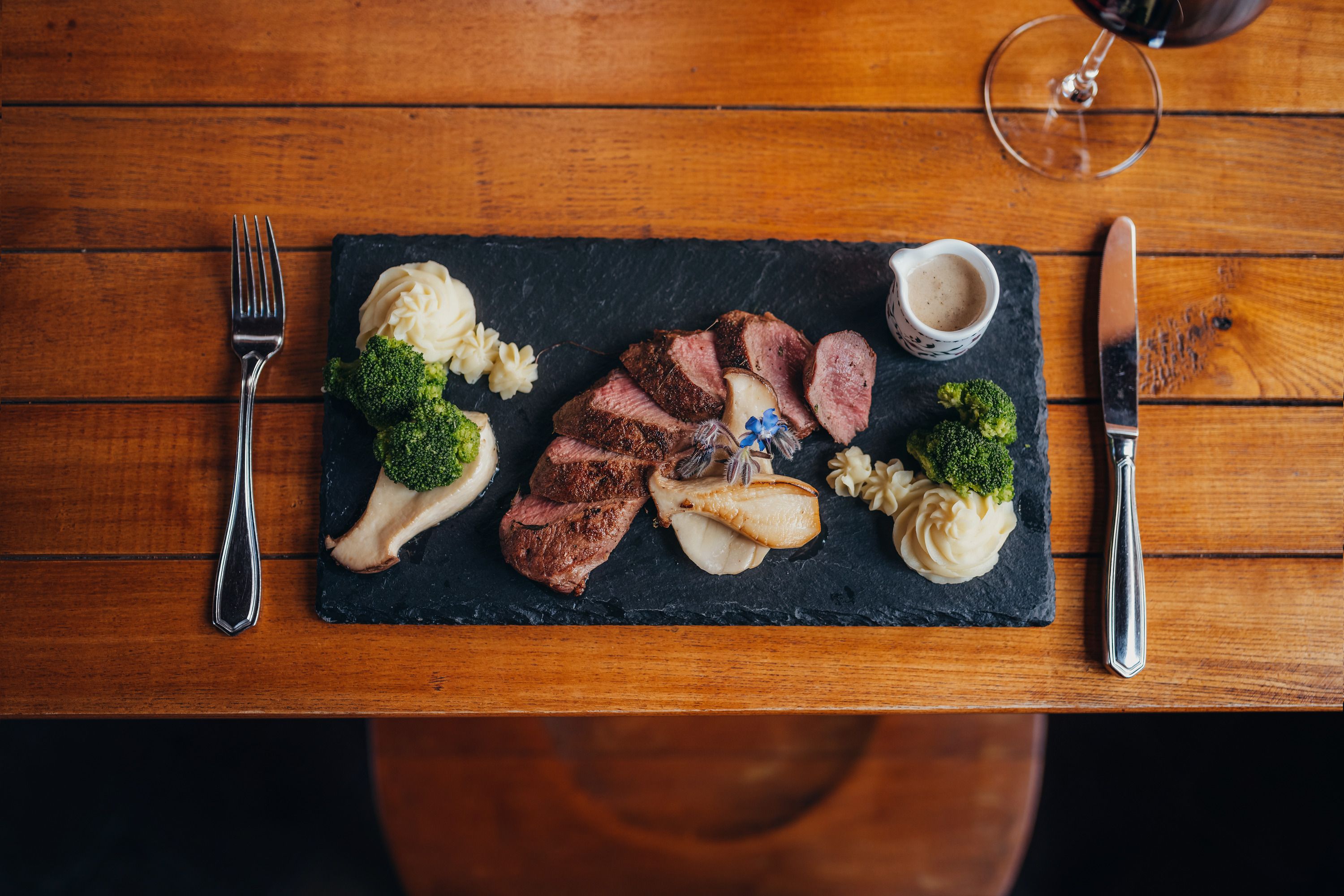 Gourmetgericht auf Schieferplatte mit Fleisch, Püree, Brokkoli und Soße.