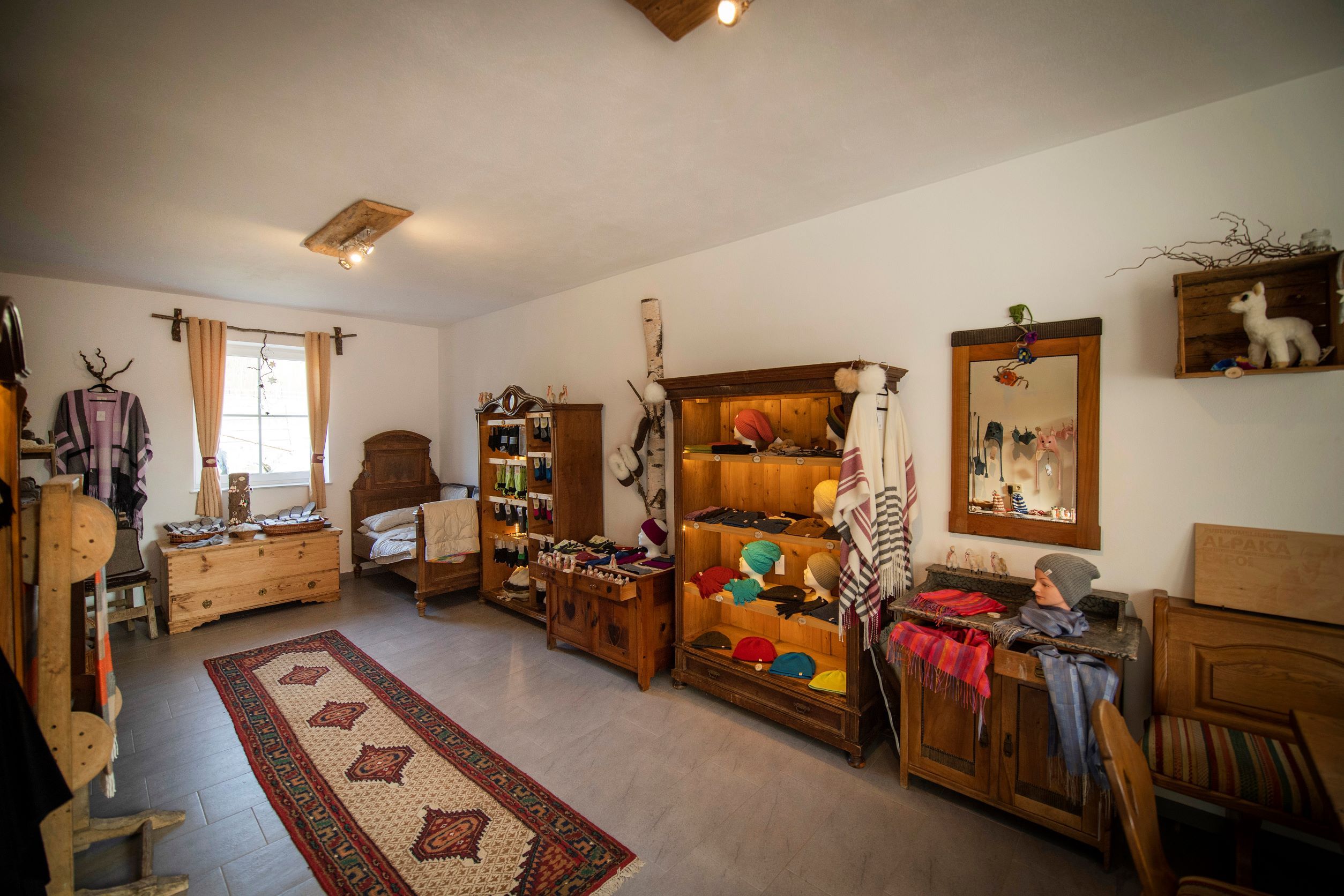Innenansicht eines Hofladens mit Alpakaprodukten, Holzmöbeln und Teppich.
