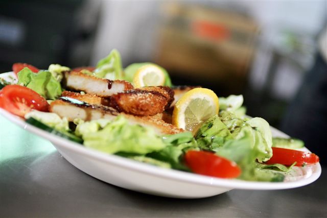 Ein Teller mit Salat, paniertem Fleisch, Tomaten und Zitronenscheiben.
