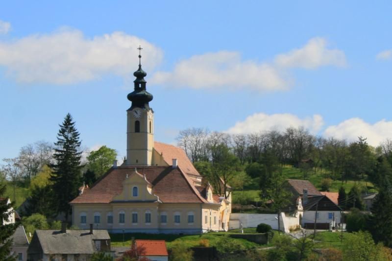 Kirche mit Turm in ländlicher Umgebung, umgeben von Bäumen und Häusern.