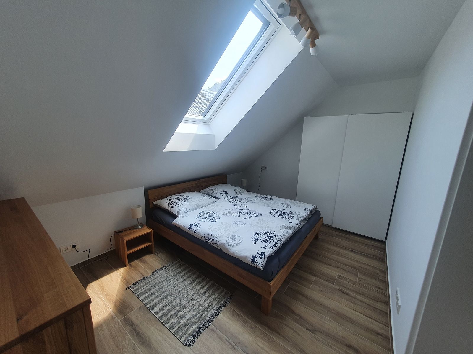 Modernes Schlafzimmer mit Dachfenster, Doppelbett, Holzmöbeln und weißem Kleiderschrank.