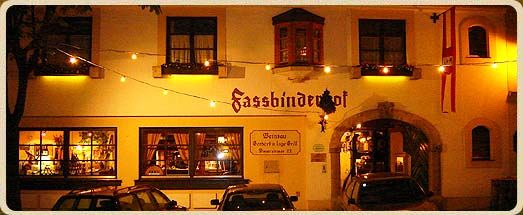 Nachtaufnahme eines Gebäudes mit der Aufschrift 'Fassbinderhof', beleuchtet von Lichterketten.