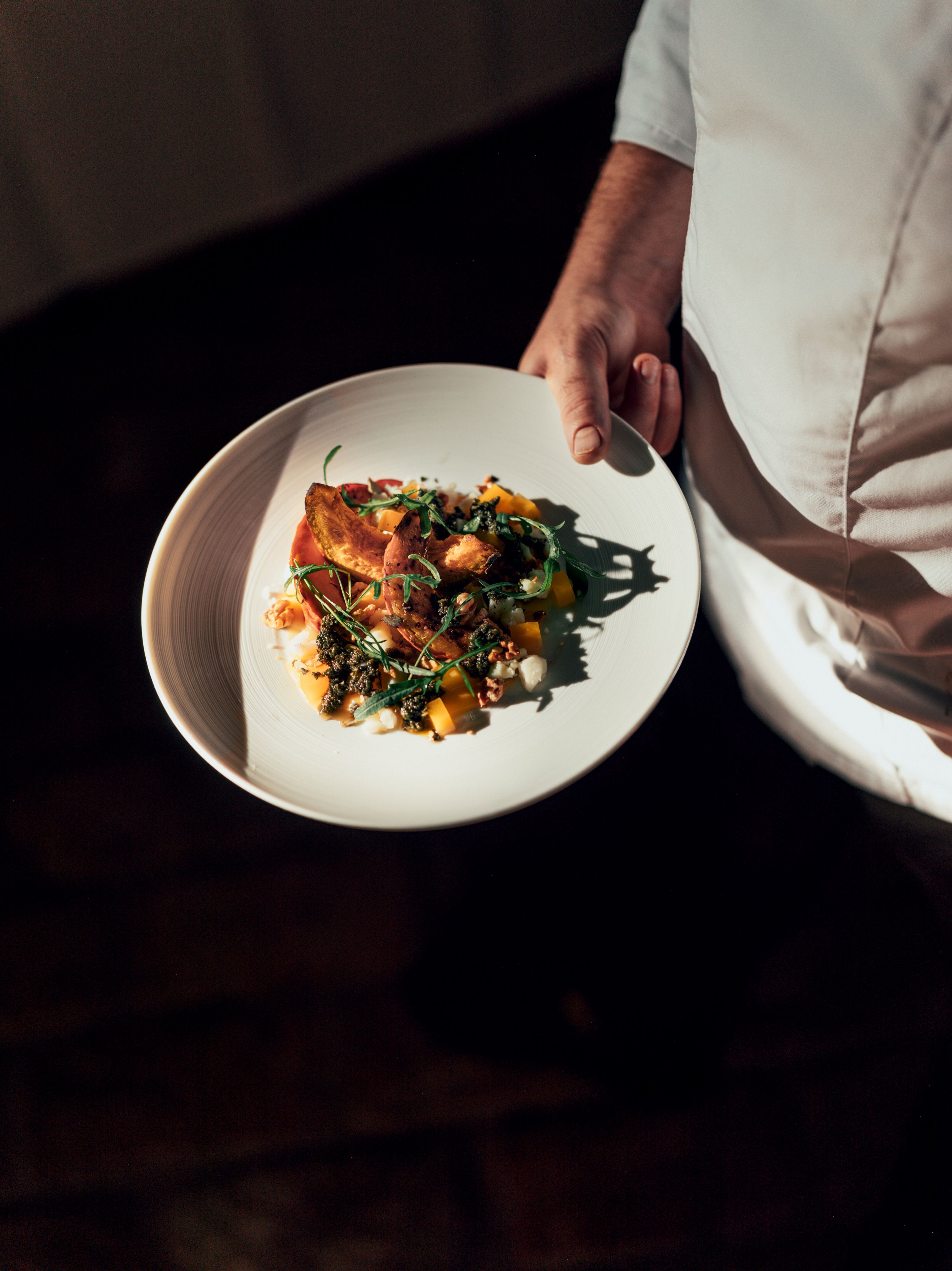 Ein Teller mit einem kunstvoll angerichteten Gericht, gehalten von einer Person in weißer Kleidung.