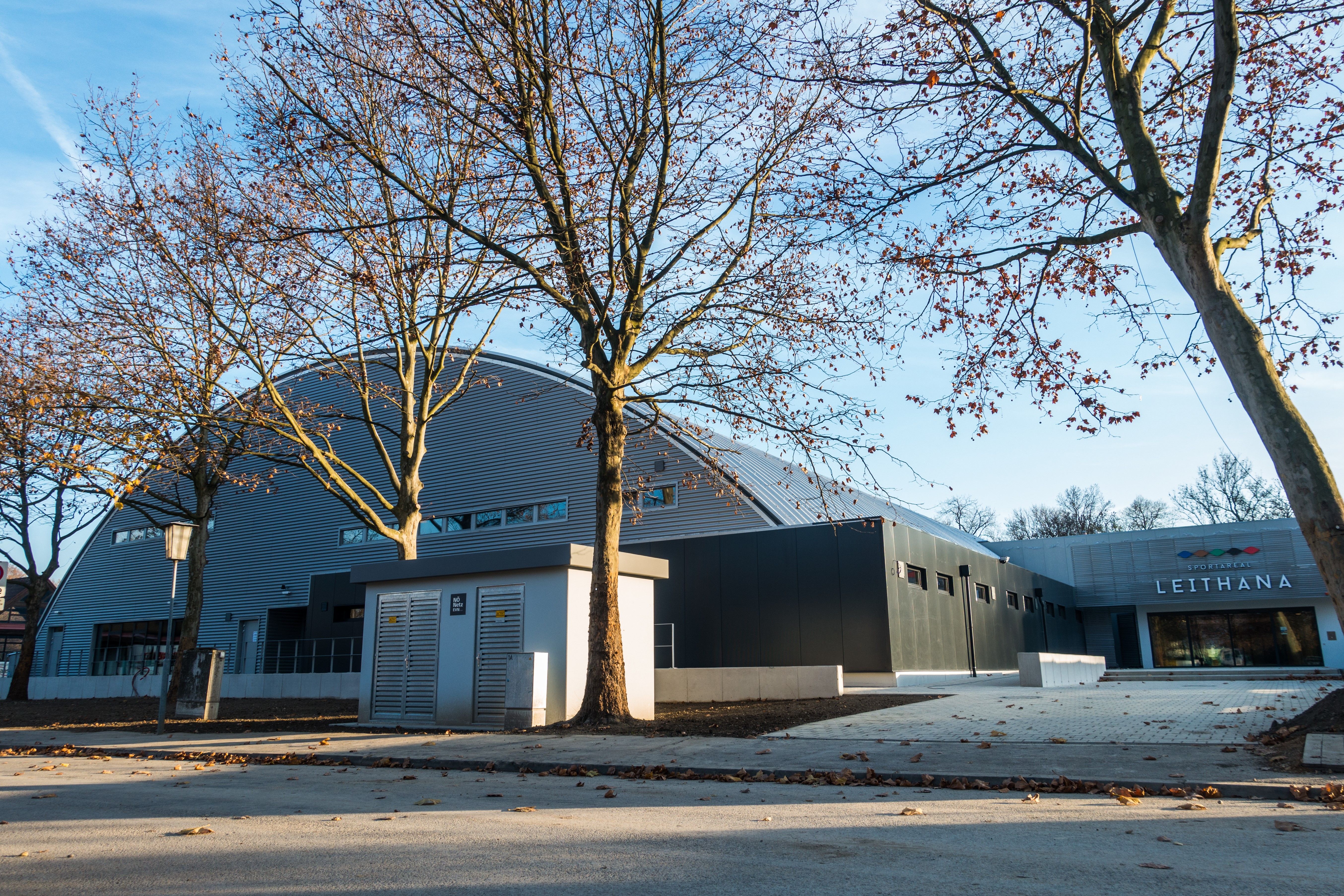 Außenansicht des Sportareals Leithana mit kahlen Bäumen im Vordergrund.