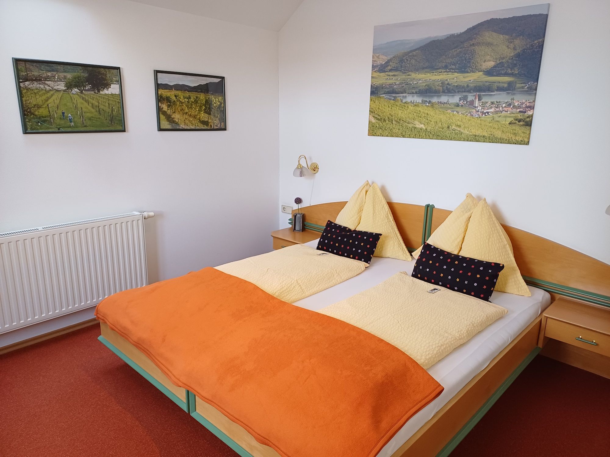 Gemütliches Hotelzimmer mit Doppelbett, orangefarbener Decke und Landschaftsbildern an der Wand.