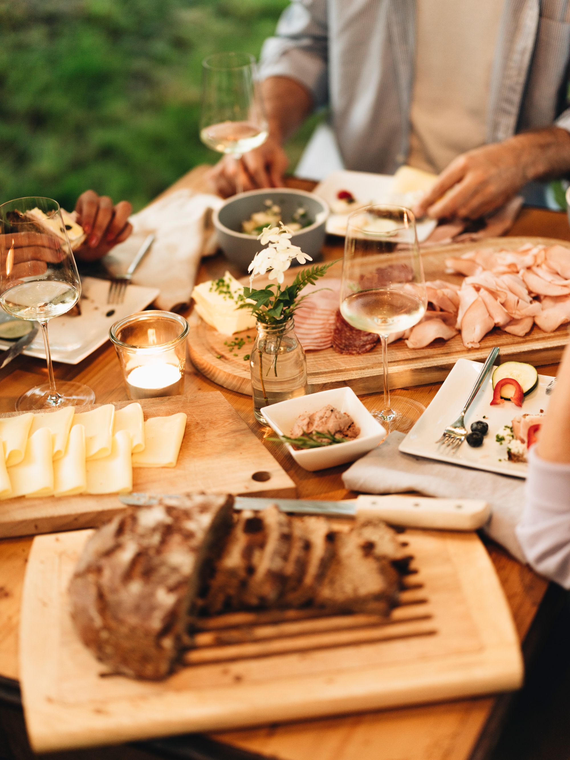 Ein gedeckter Tisch mit Brot, Käse, Aufschnitt und Weingläsern im Freien.
