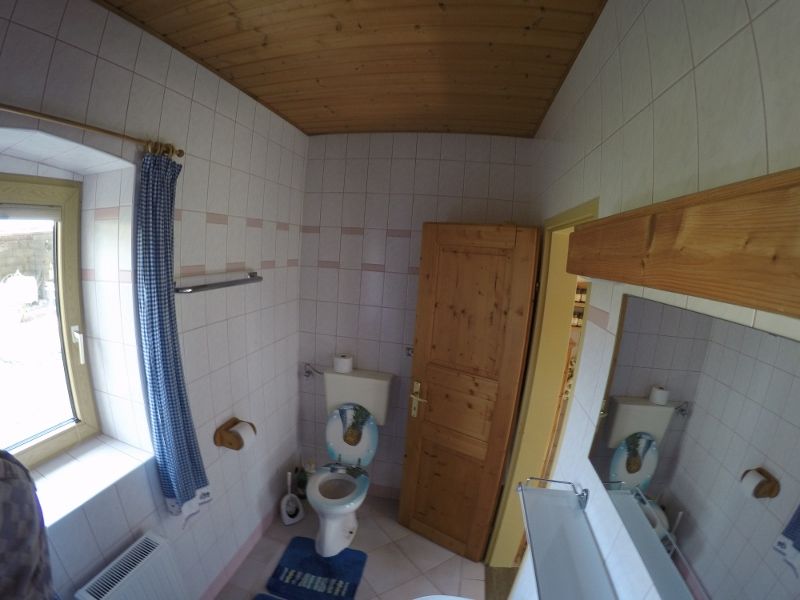 Badezimmer mit Toilette, Holzdecke und Fenster mit blauem Vorhang.