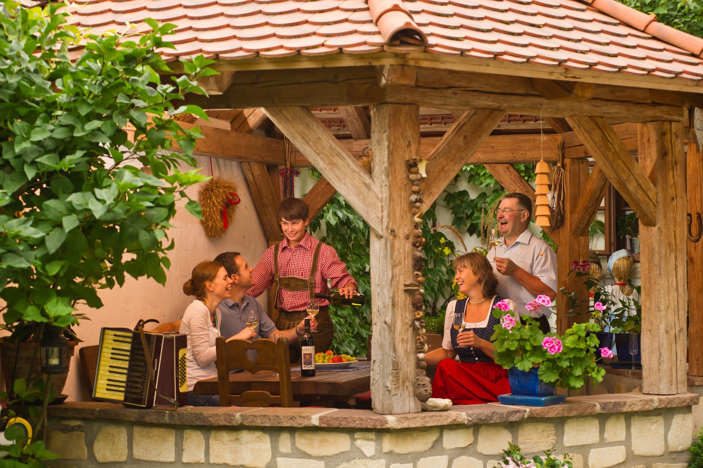 Eine Gruppe von Menschen sitzt in einem überdachten, rustikalen Pavillon und genießt Wein und Gesellschaft.