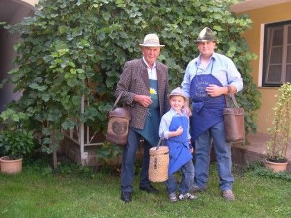 Drei Generationen von Männern in traditioneller Kleidung mit Körben im Garten.
