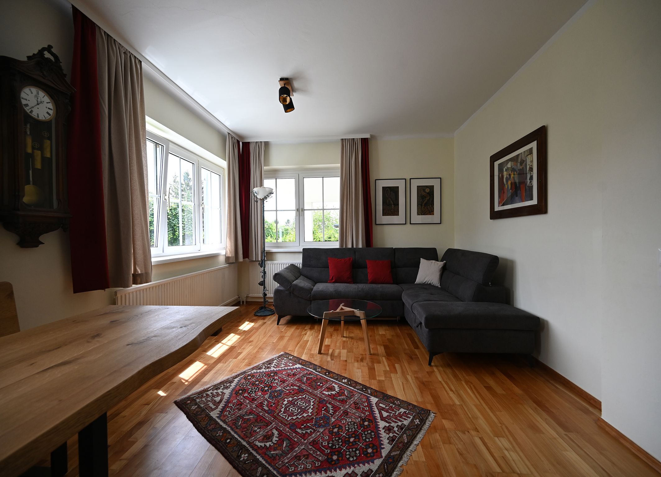 Modernes Wohnzimmer mit grauem Sofa, Holztisch, Teppich und Wanduhren.