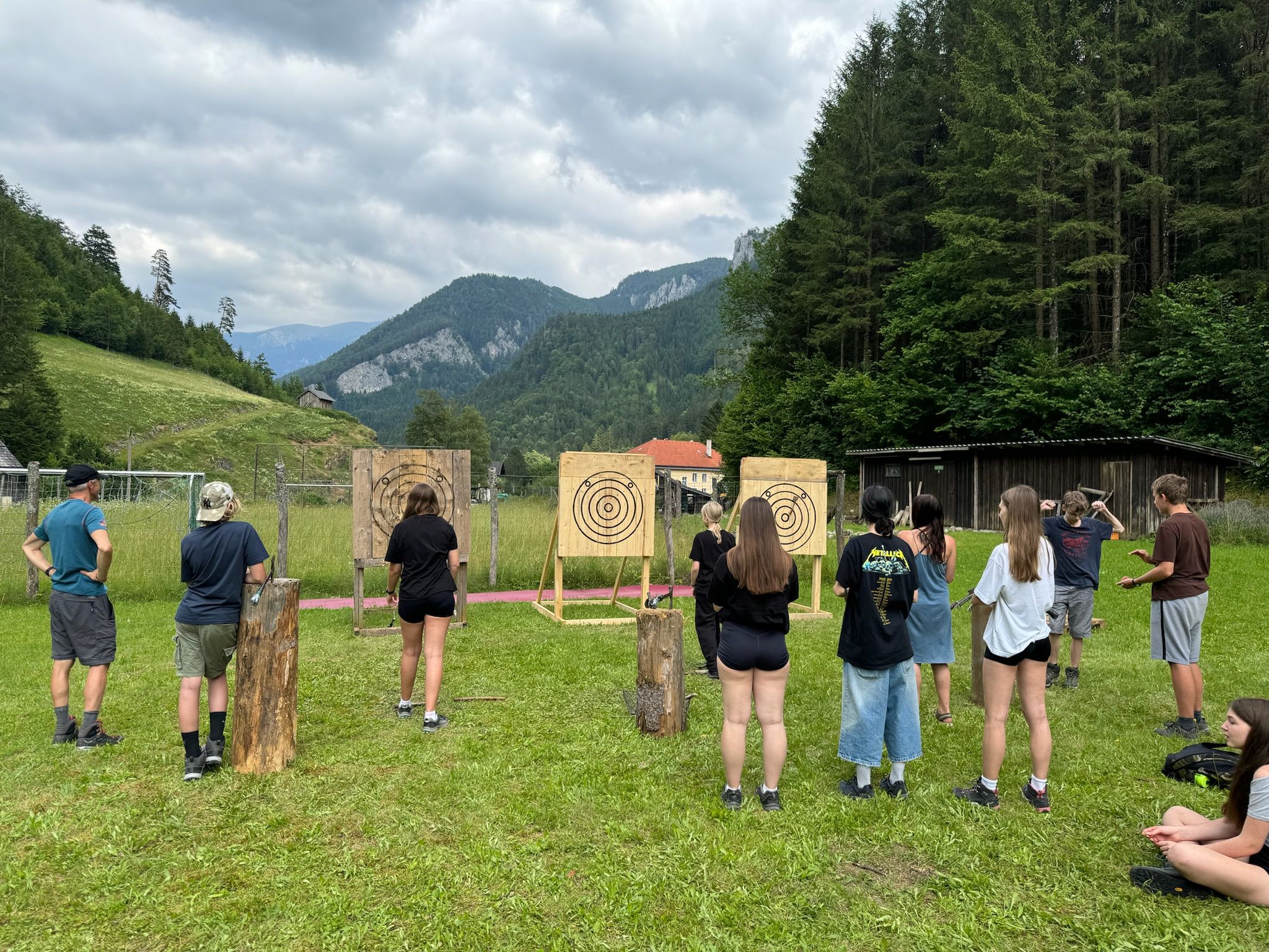 Gruppe von Menschen beim Axtwerfen im Freien vor Zielscheiben in einer bergigen Landschaft.